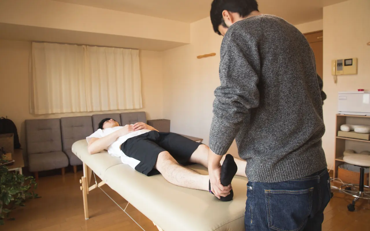 Fisioterapeuta a mobilizar a perna de um utente deitado numa marquesa, em casa